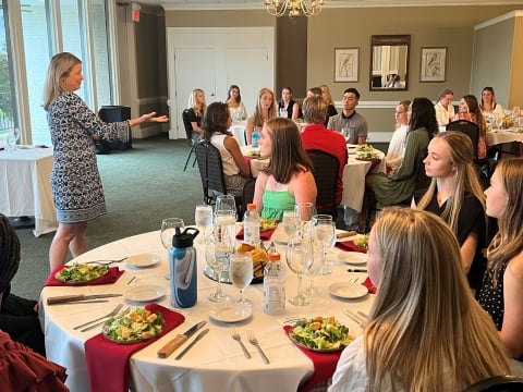 Student athletes sit at tables with white tablecloths, learning proper etiquette for a formal dinner