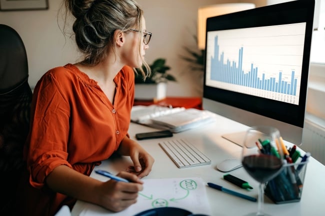 Woman sits at computer looking at data visualizations and taking notes