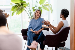 White woman listening with focus to a Black woman as they sit in chairs together