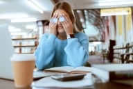 Woman student with glasses, stress with headache and burnout, tired about paper deadline or study for exam in library