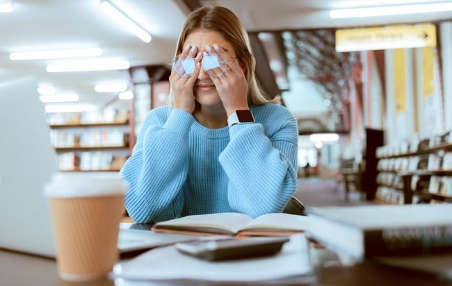 Woman student with glasses, stress with headache and burnout, tired about paper deadline or study for exam in library