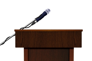 A wooden speaker podium and microphone, against a white background, with no speaker behind it.