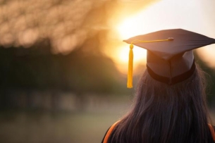 Photo of graduate wearing a mortar board with a sunset in the background.