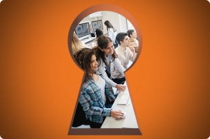 Students sit in a computer lab as seen through a keyhole.