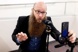 Christopher Clarke films a vertical video using his cellphone and a microphone on a stand.