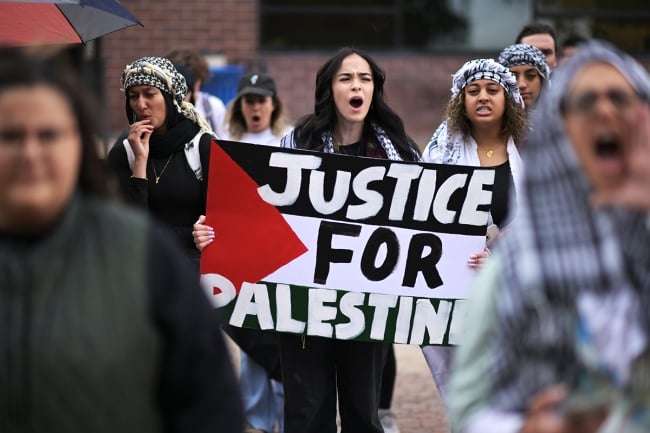 A group of protesters with a woman in the center holding a banner that says "Justice for Palestine"