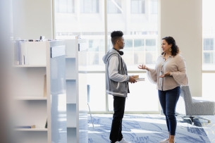 A student speaks with a professor holding a stack of books