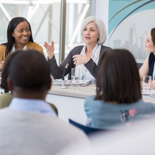 A professional-looking woman sits on a panel addressing an audience.