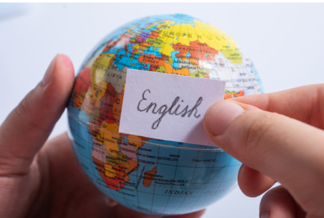 A close-up of a person's hands holding a globe along with a scrap of paper that says, in cursive, "English."