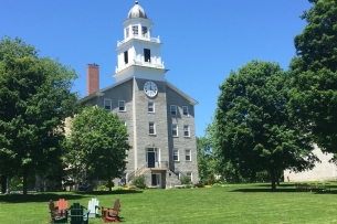 Middlebury's stone chapel in front of a blue sky. In the foreground, lawn chairs sit in a circle on the grass.