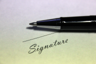 A pen atop a piece of paper next to a blank space for a signature.